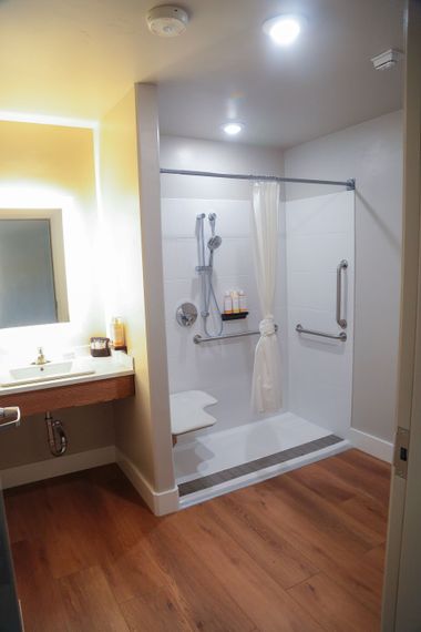 Accessible bathroom with a roll-in shower, white tile, and wood flooring