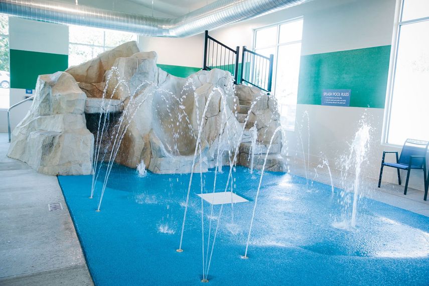 Indoor pool with blue water, rock formation, and water jets spraying in a bright room