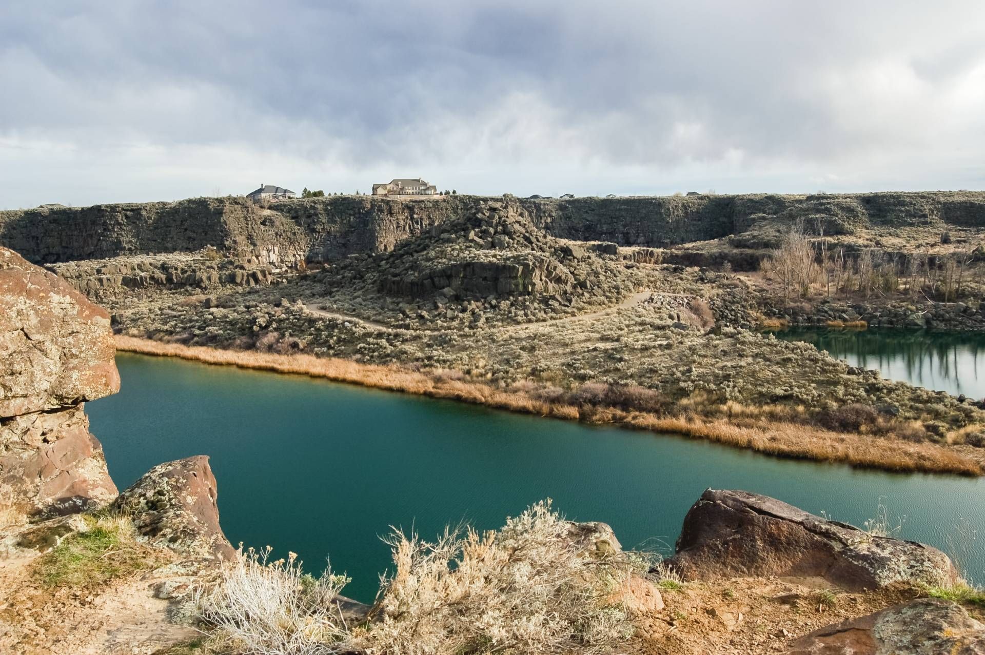 A blue lake winds through a rocky canyon under a cloudy sky.