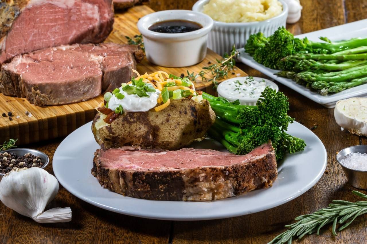 Prime rib dinner with a baked potato, vegetables, and gravy.