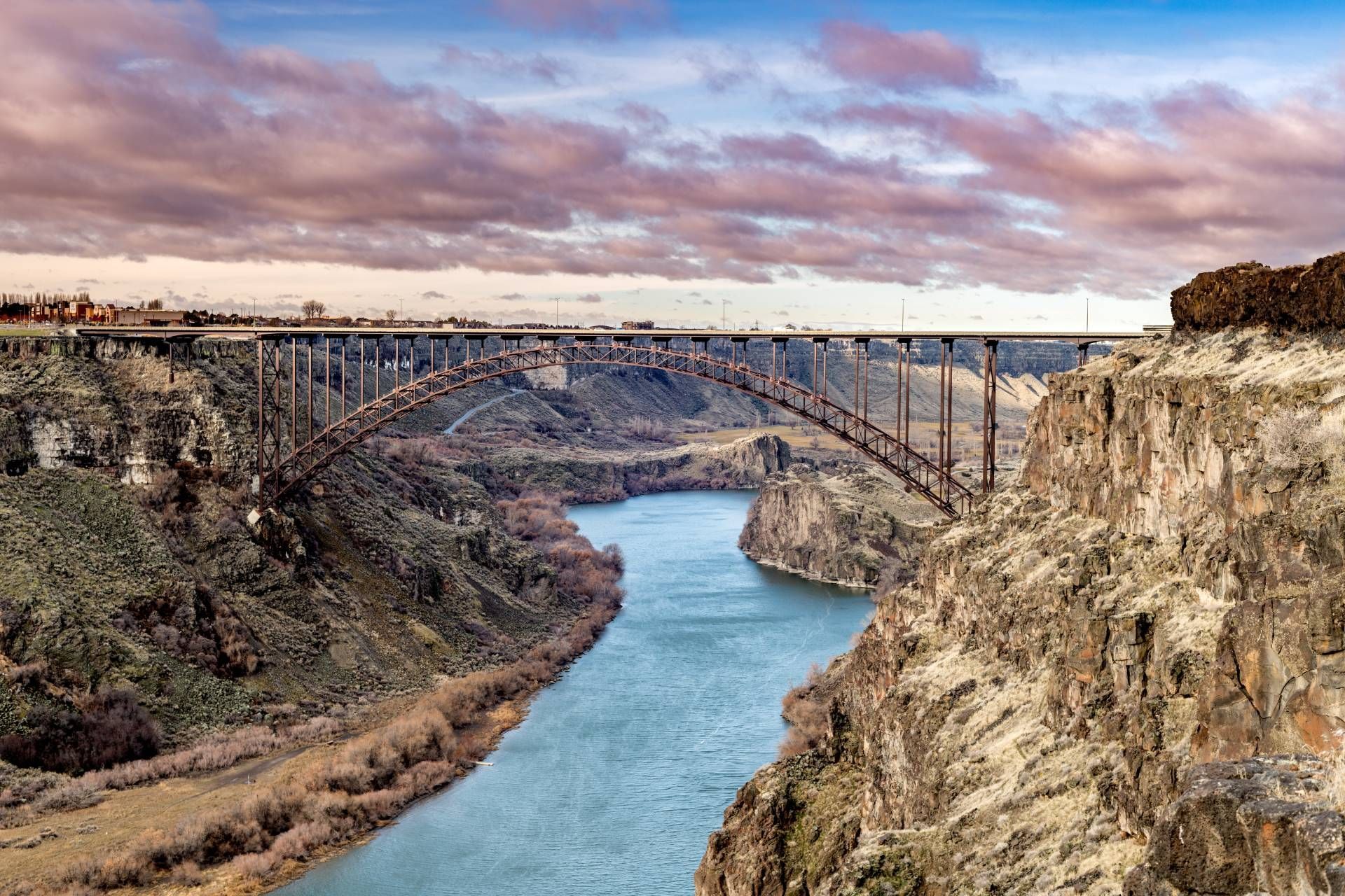 A large arched bridge spans a canyon with a river below; cloudy sky.