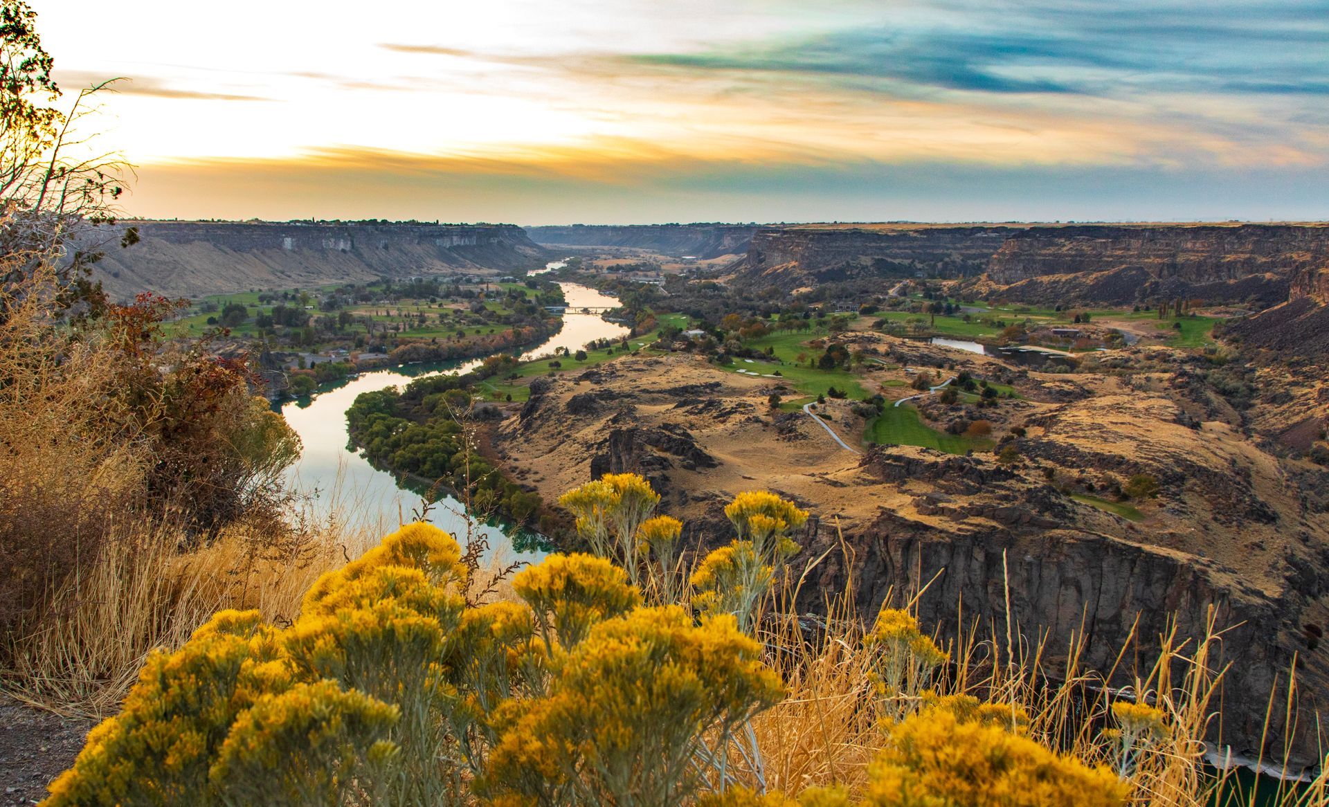 Canyon landscape with a winding river at sunset; golden brush in foreground, cliffs on either side.