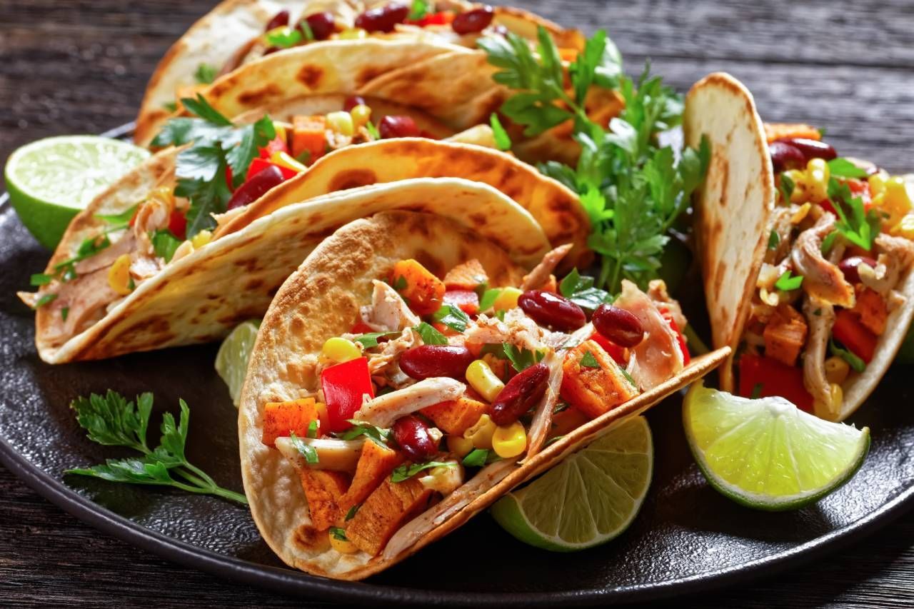 Plate of colorful tacos with various fillings, lime wedges, and parsley.