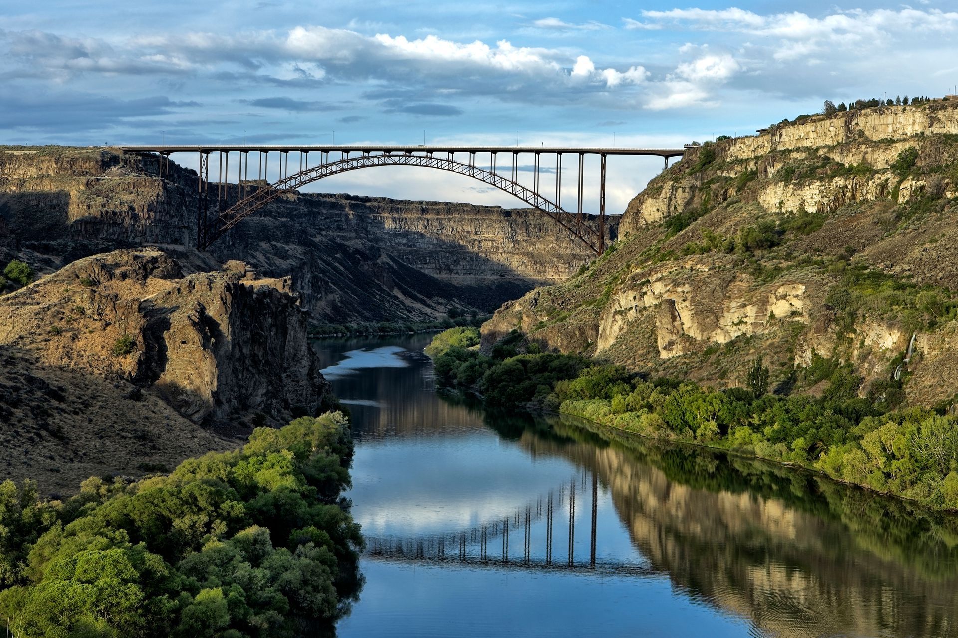 A bridge arches over a river between canyon walls; trees line the riverbanks.