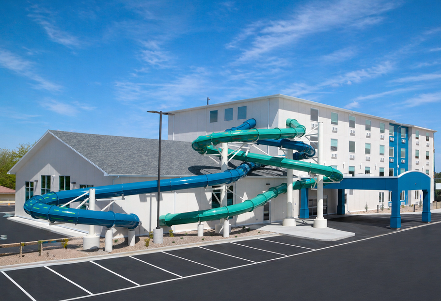 Outdoor water slide complex with teal slides beside a white hotel building under a blue sky