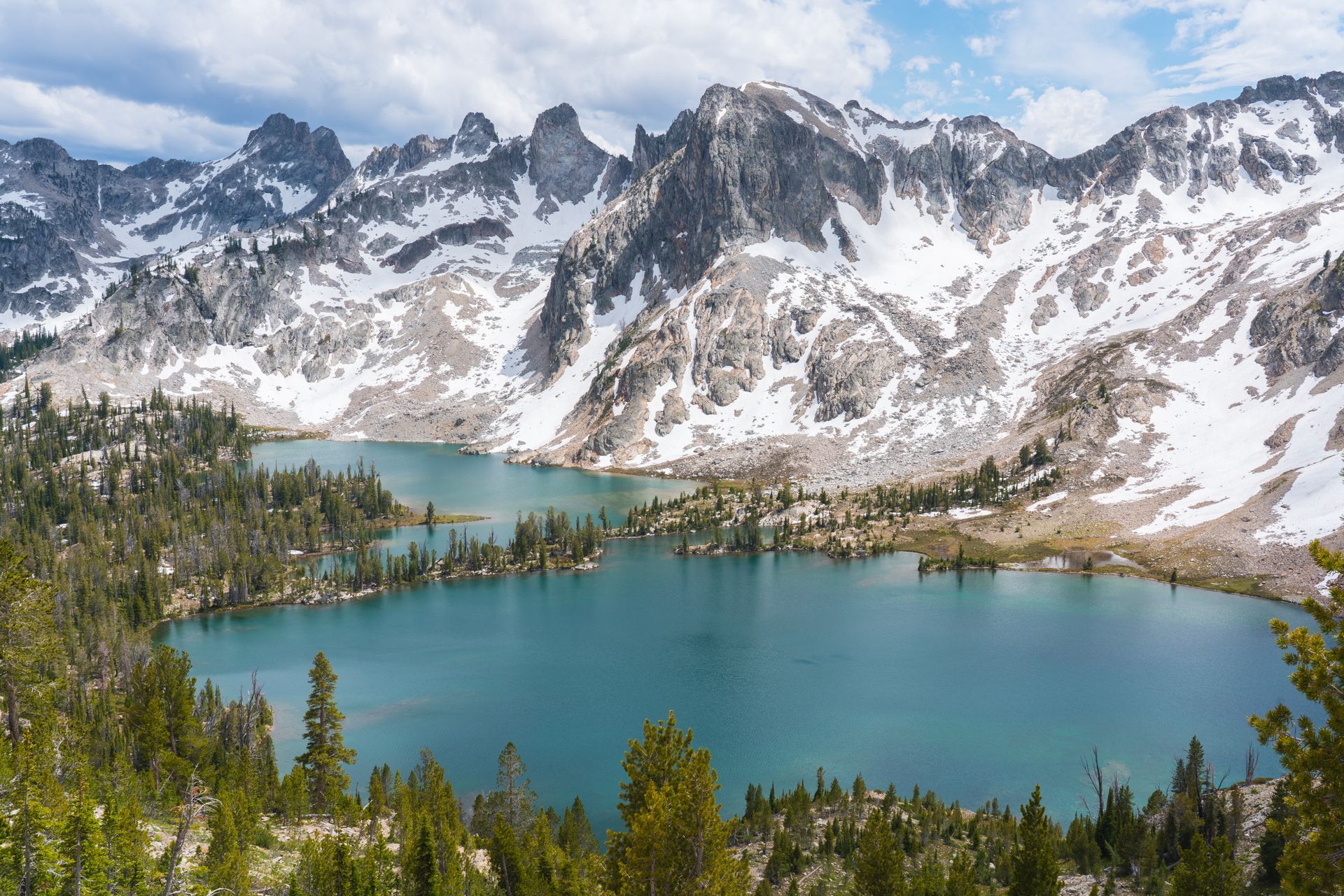 Turquoise alpine lake surrounded by snowy mountains and pine forest under a clear sky