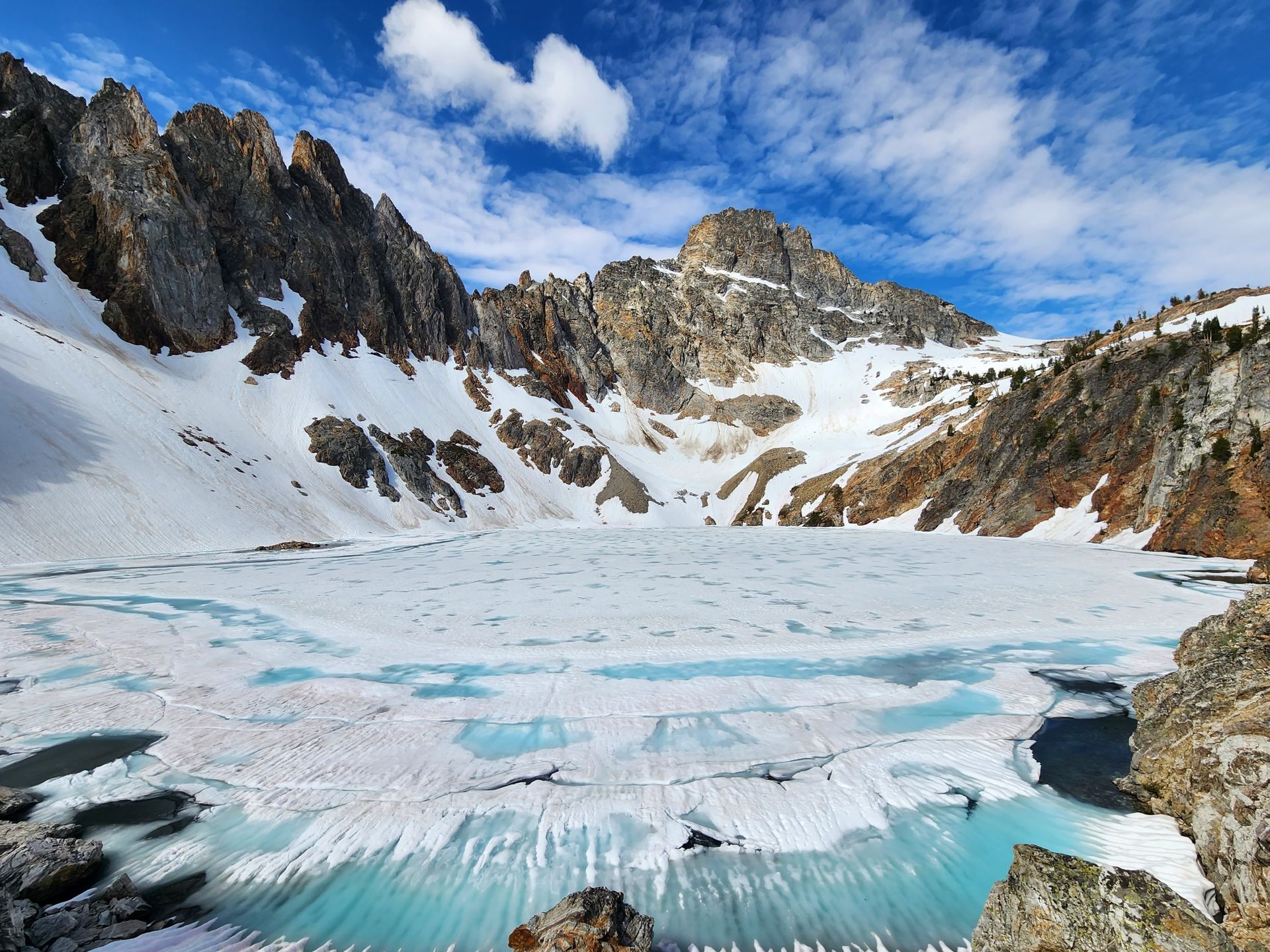 Snowy mountain lake with blue ice, jagged peaks, and a bright cloudy sky