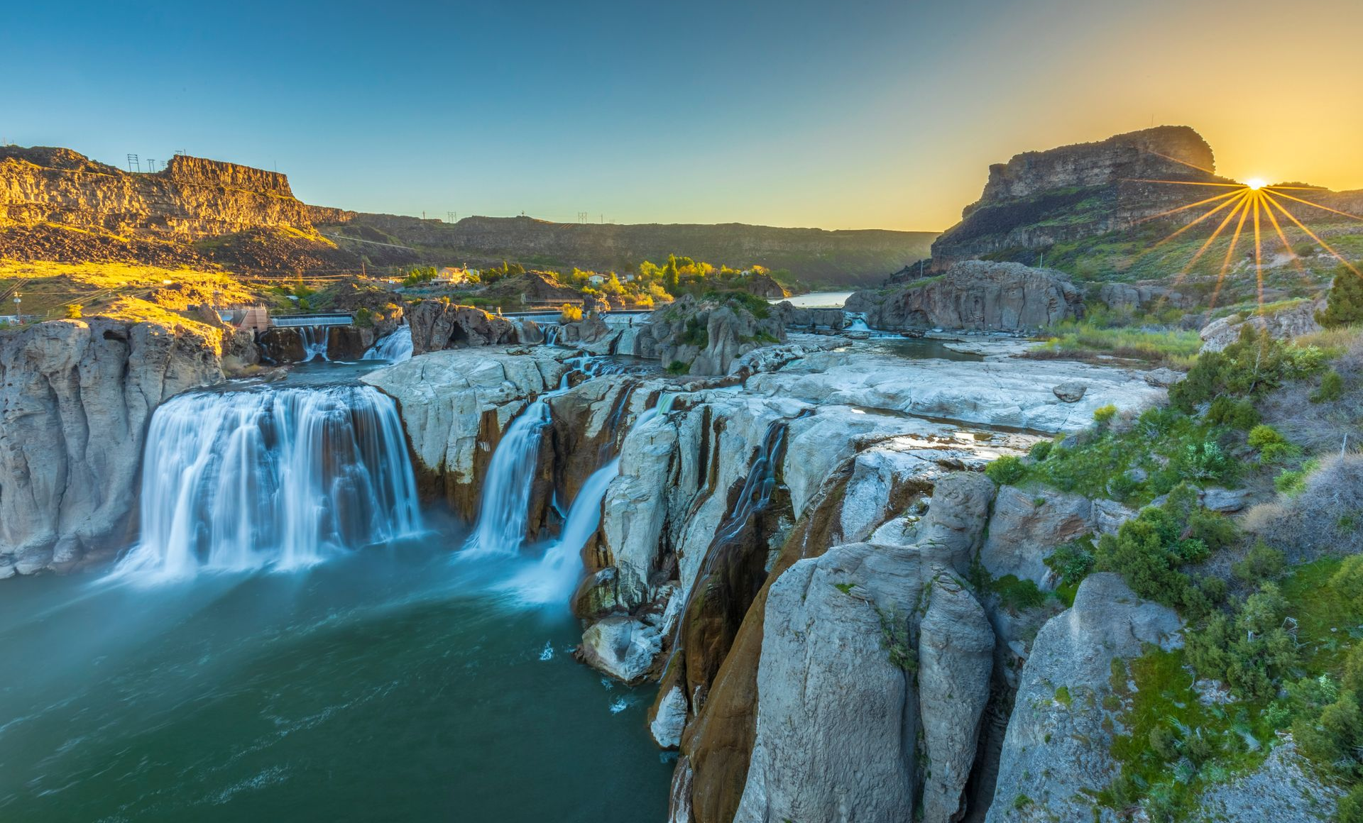Sunset over a wide waterfall cascading into a rocky river canyon