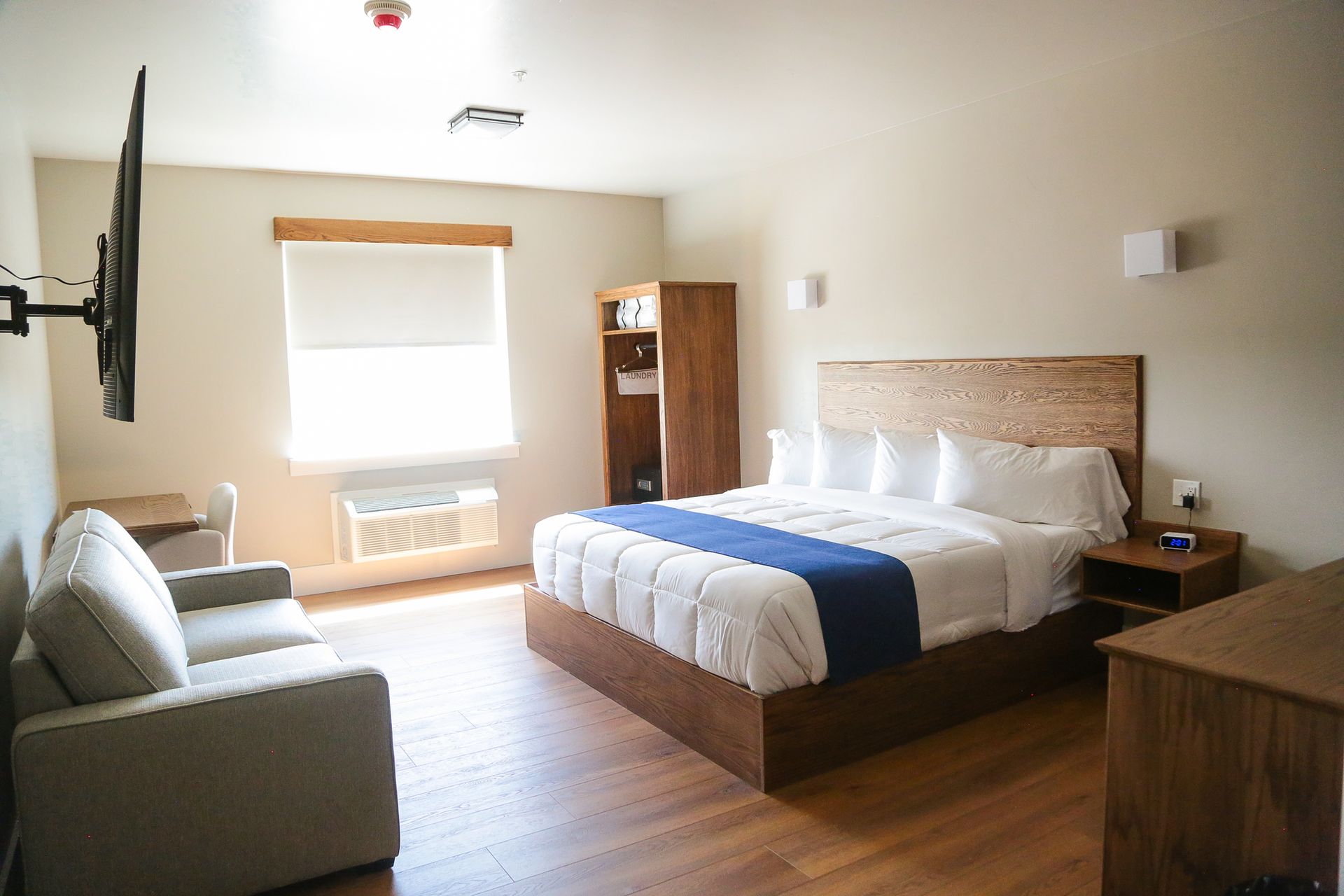 Bright hotel room with a bed, sofa, desk, and window in warm daylight
