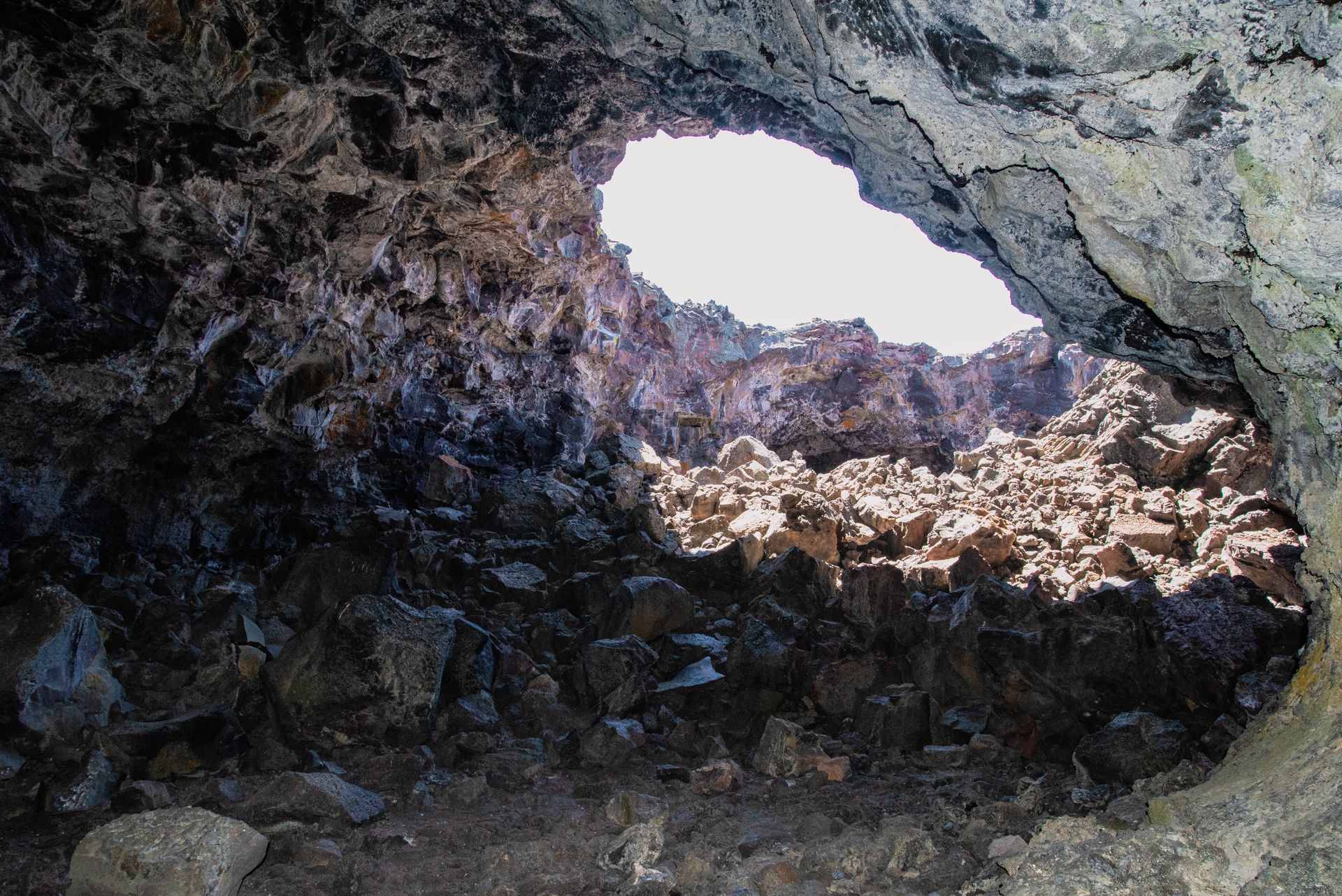 View from inside a rocky cave opening onto bright daylight and jagged volcanic rocks outside