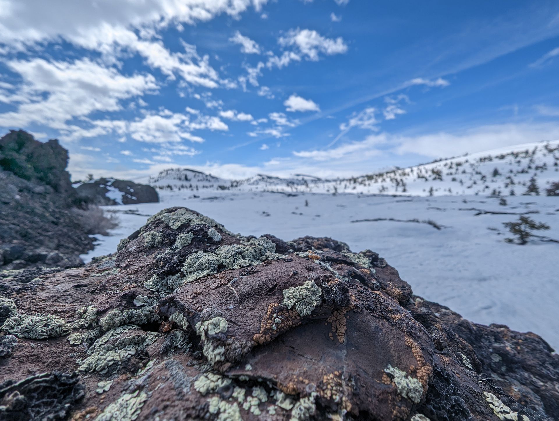 Snowy mountain landscape with lichen-covered rocks under a blue sky with scattered clouds