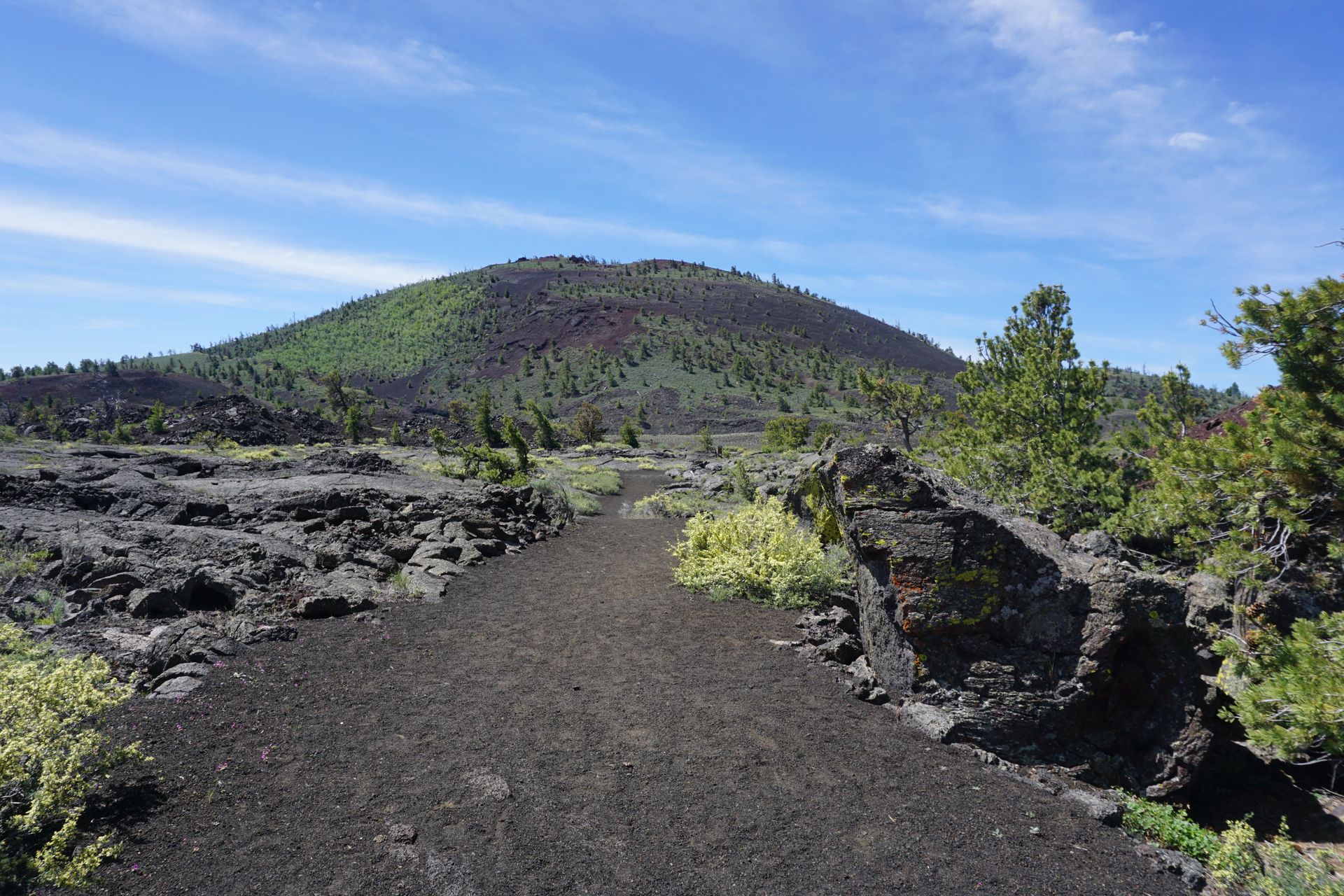 Volcanic trail leading toward a green cinder cone under a blue sky