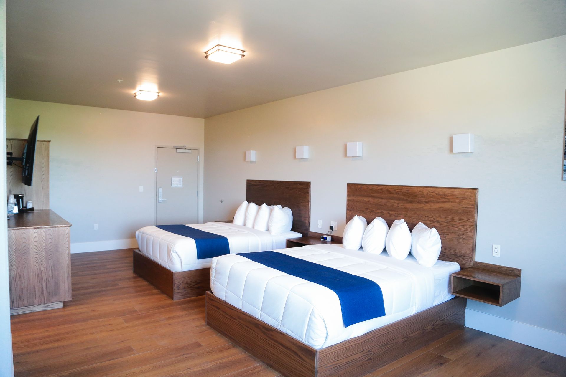 Modern hotel room with two neatly made beds, blue runners, and warm wood flooring