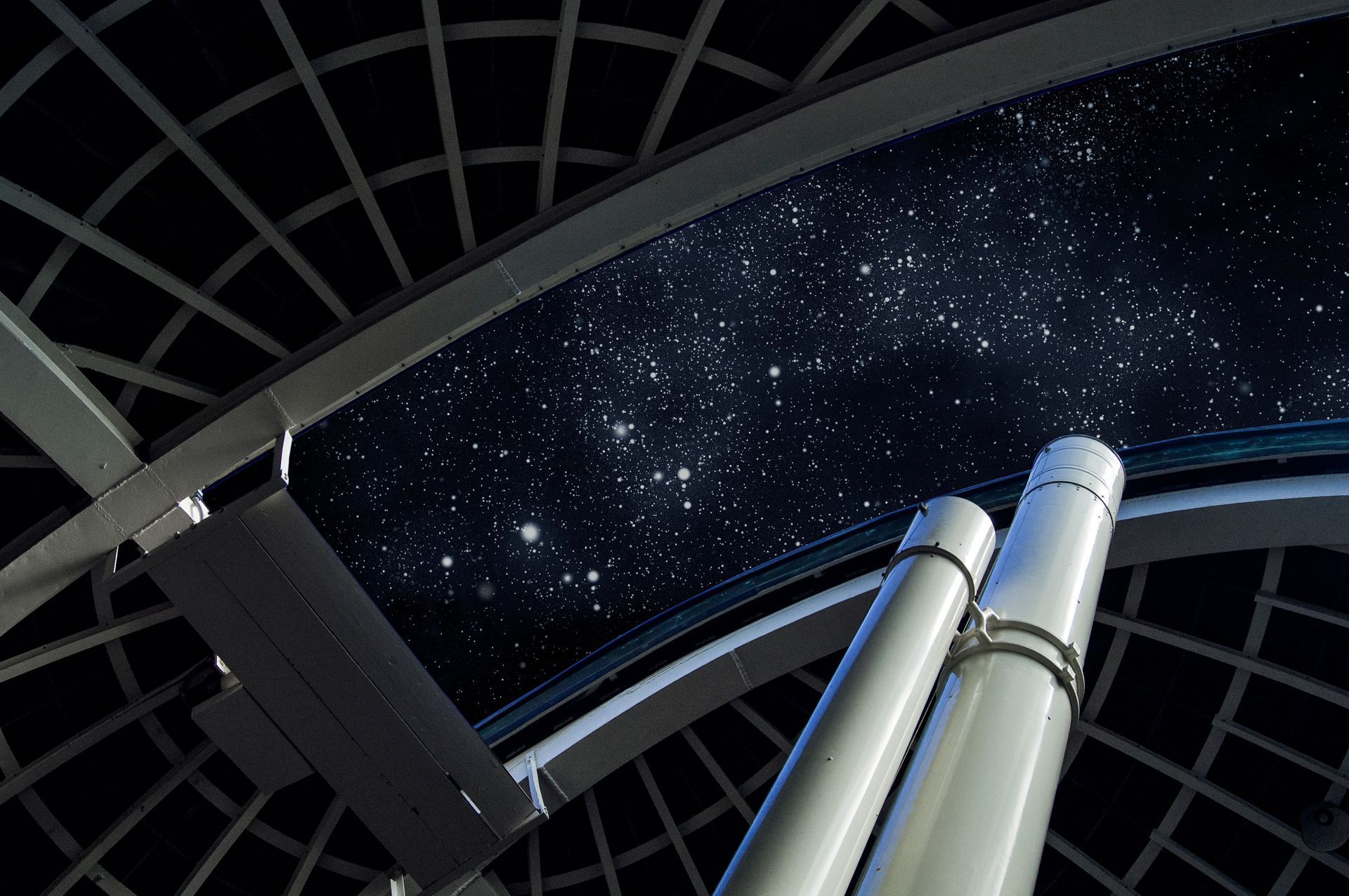 Two silver telescopes beneath a domed observatory roof, pointed at a starry night sky.