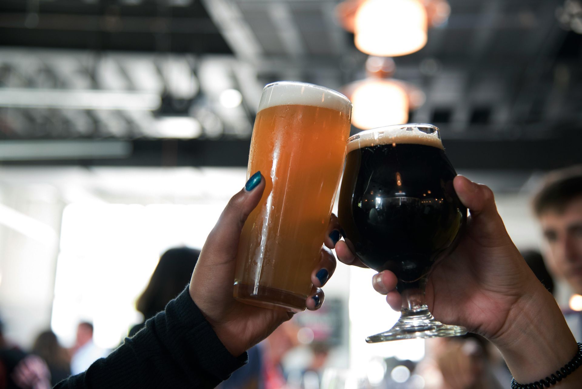 Two hands toasting with glasses of light and dark beer in a bar setting.
