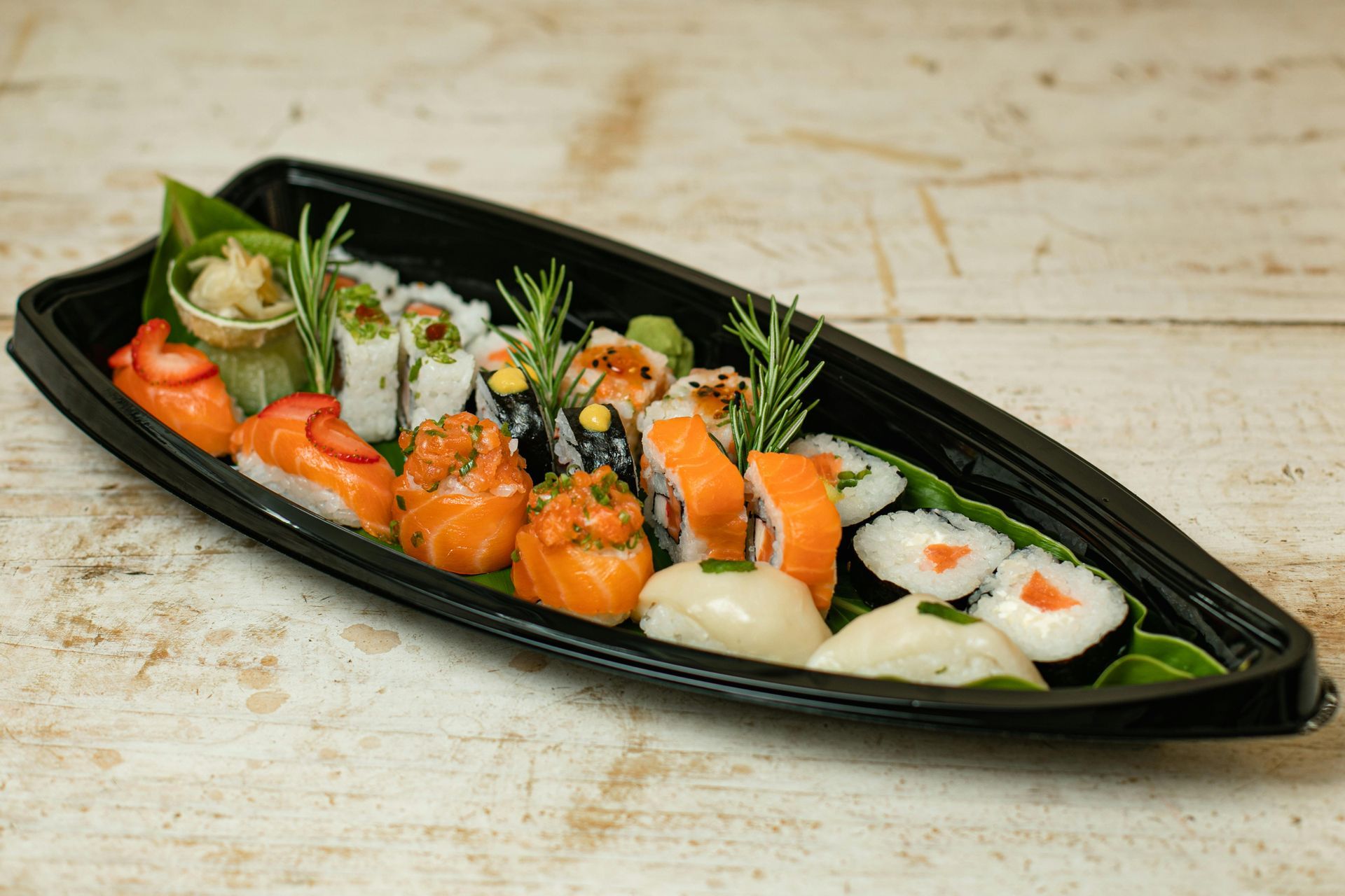 Sushi platter with various rolls, nigiri, and garnishes, served in a black boat-shaped container.