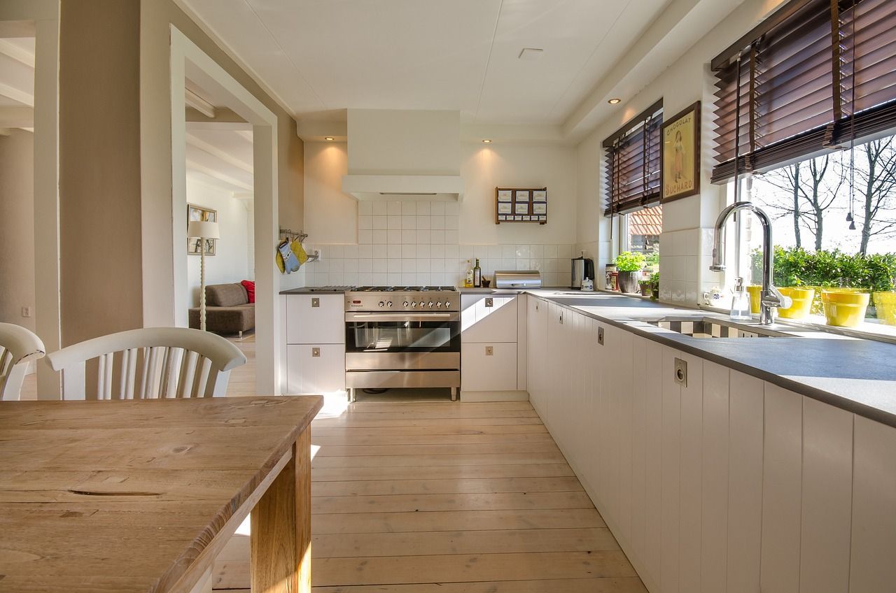 Bright white kitchen with wooden floor, long countertop, and window blinds above a sink.