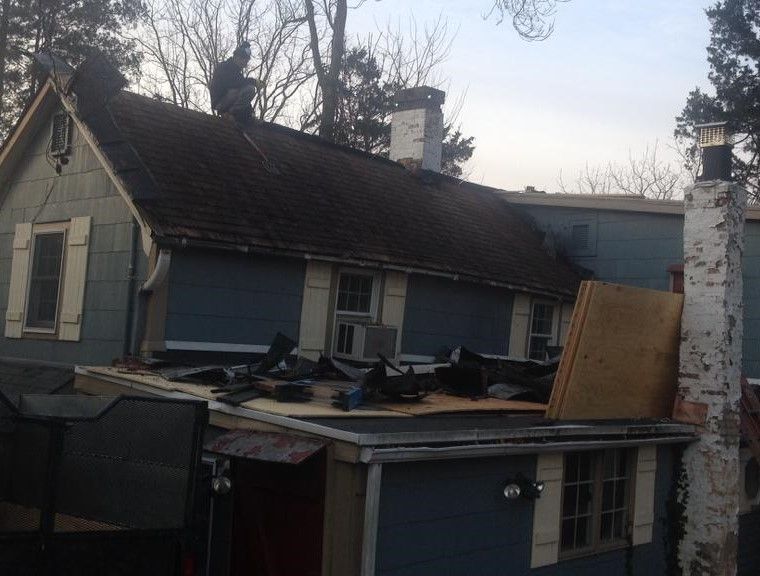 Damaged blue house with a collapsed roof and chimney, seen from outside at dusk
