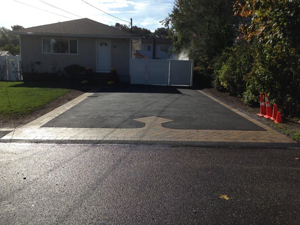 Driveway leading to a small house with a white gate, bordered by grass and orange cones.
