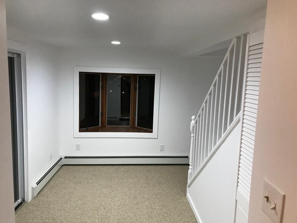 Empty carpeted room with white walls, window, and staircase railing