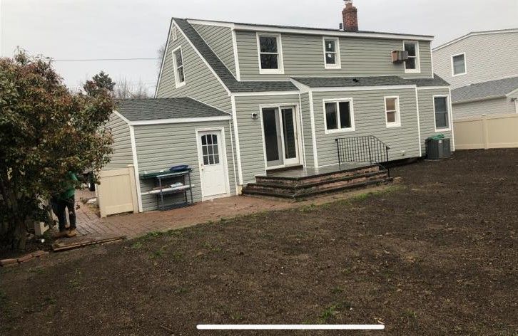 Gray house with white trim and small porch beside a muddy backyard under an overcast sky