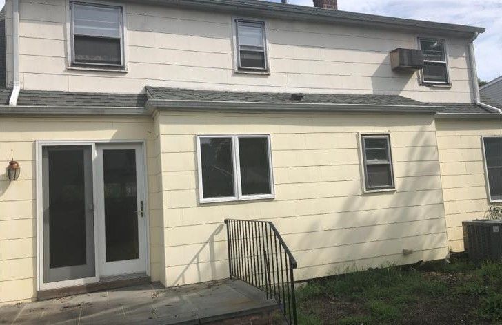 Back of a beige two-story house with a sliding glass door and small deck steps