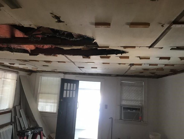 Damaged room ceiling with large holes and exposed insulation above a doorway and windows