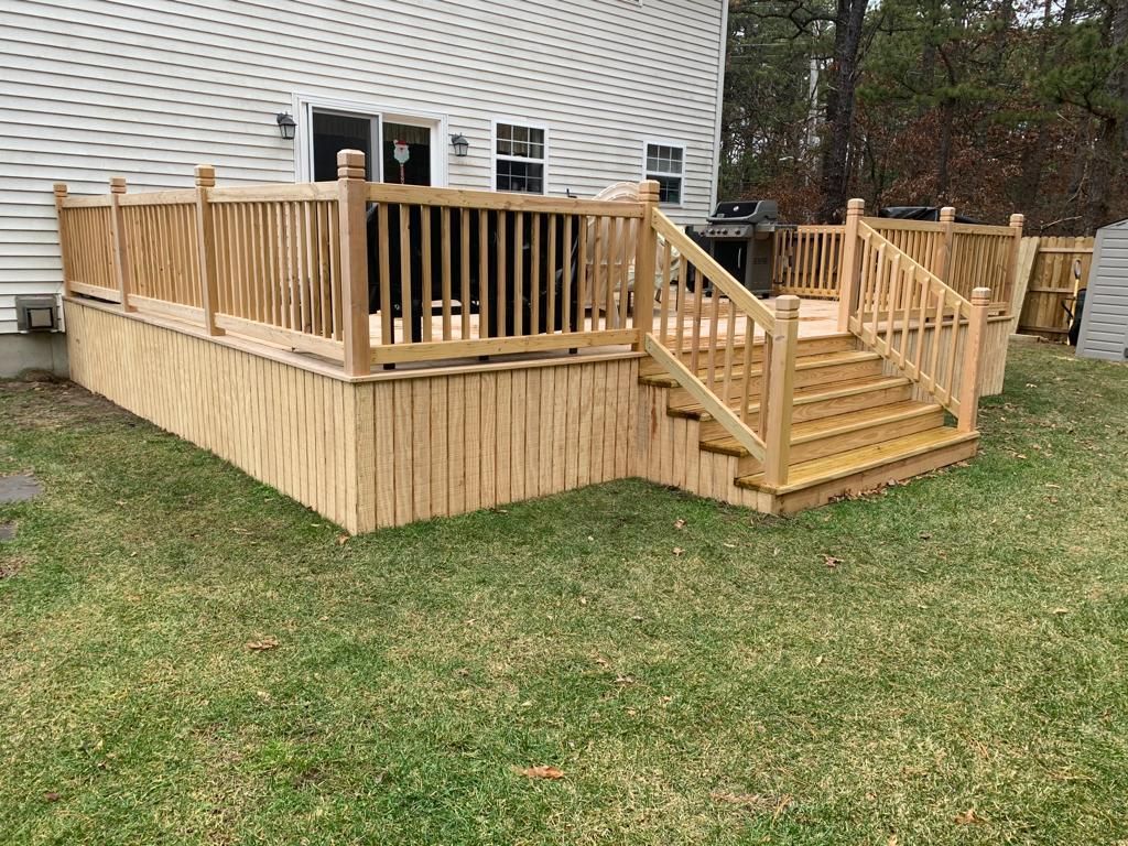 Wooden backyard deck with railing and stairs beside a house, set on a grassy lawn.