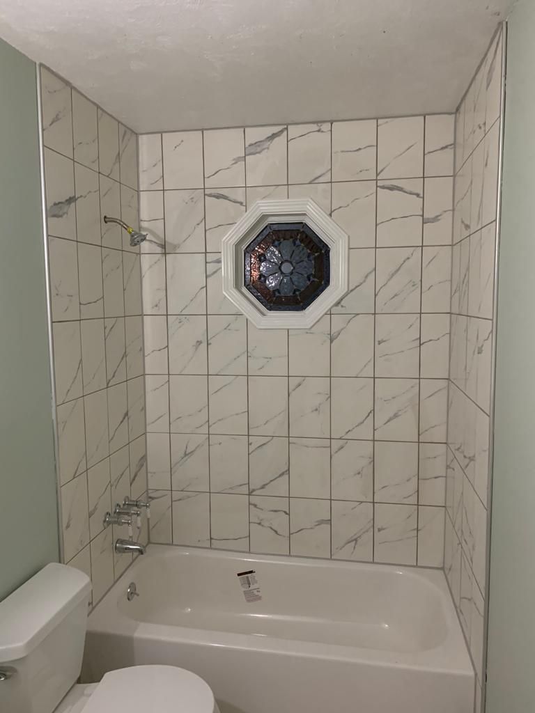 Small bathroom with tiled walls, a bathtub, and an octagonal window above the tub.