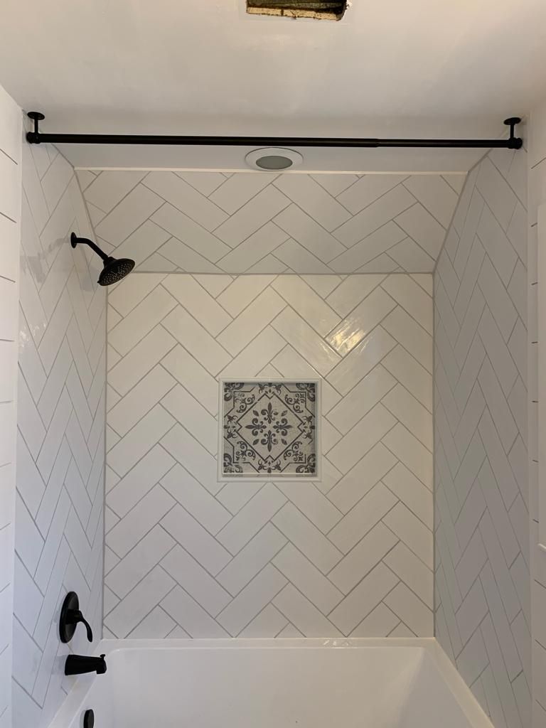 White tiled shower with black fixtures and a square mosaic accent tile.