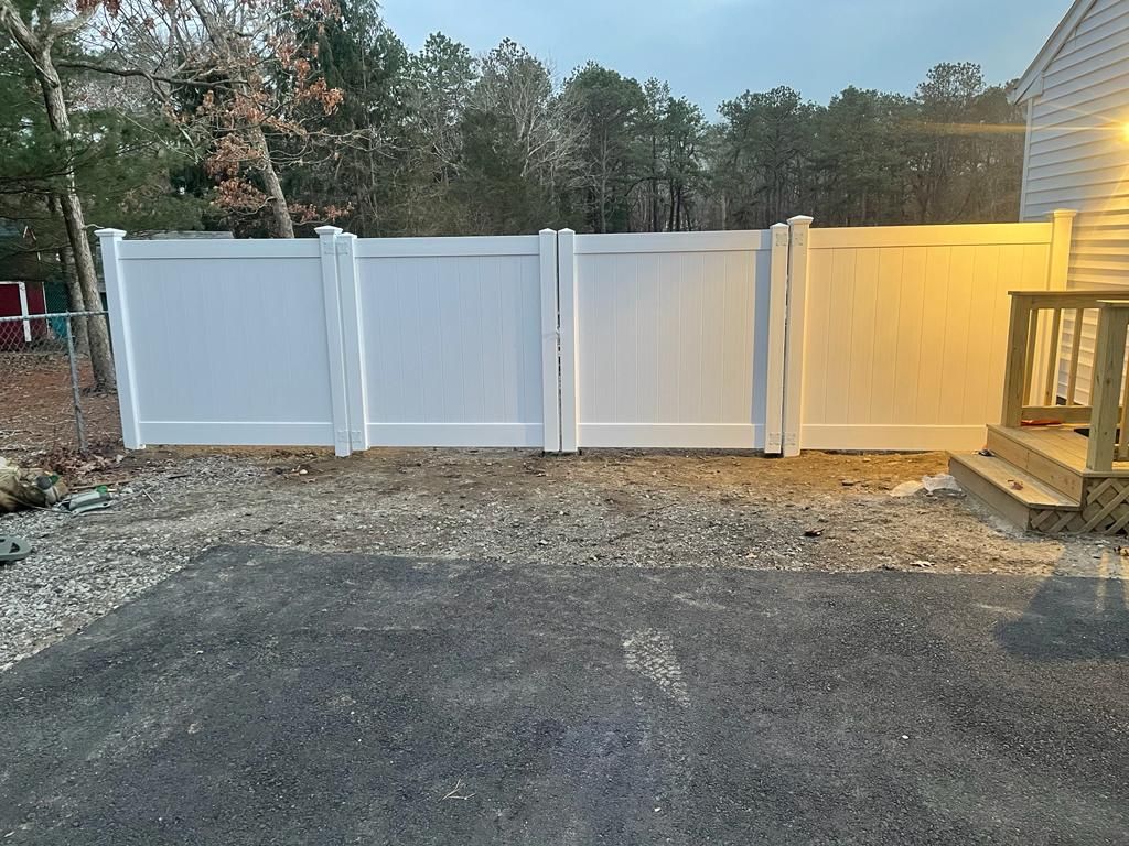 White vinyl privacy fence along a gravel driveway beside a wooden deck at dusk