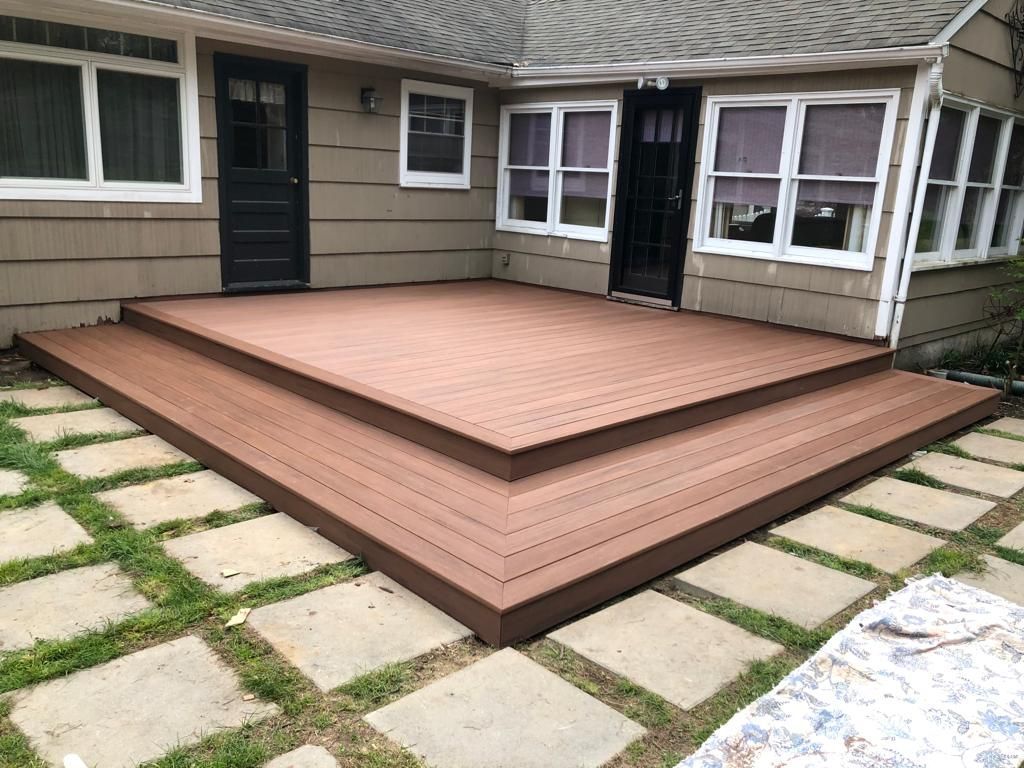 Raised brown wooden deck in a backyard patio with a house and stepping stones around it