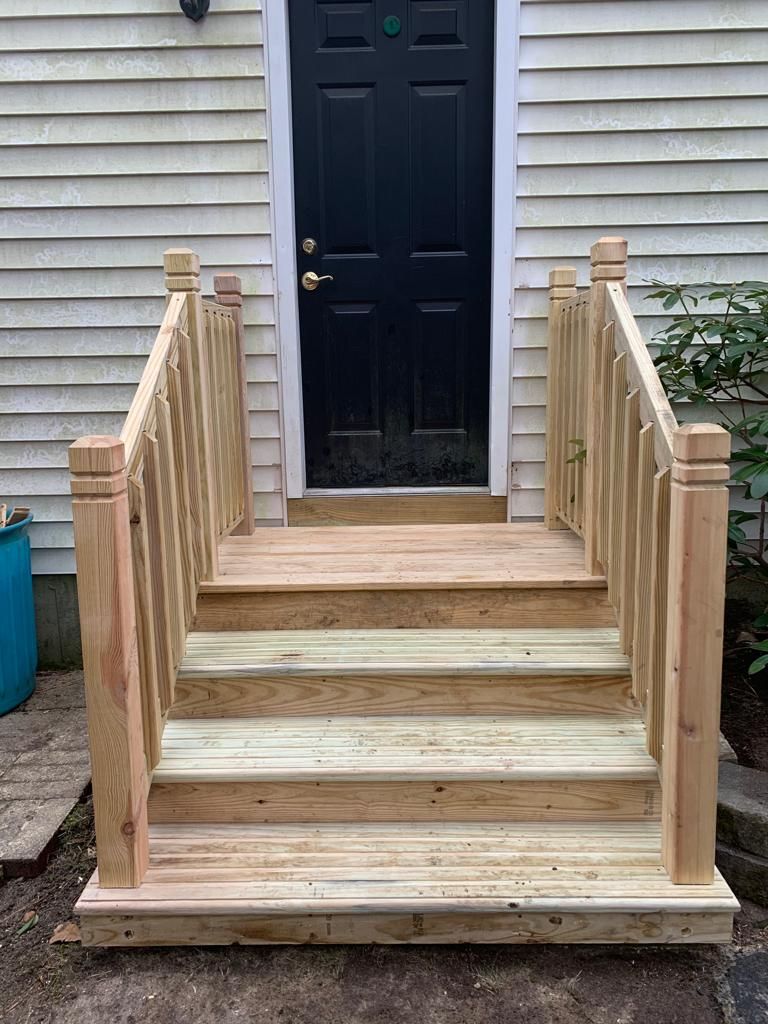 Wooden front steps with railings leading to a black door on a house exterior