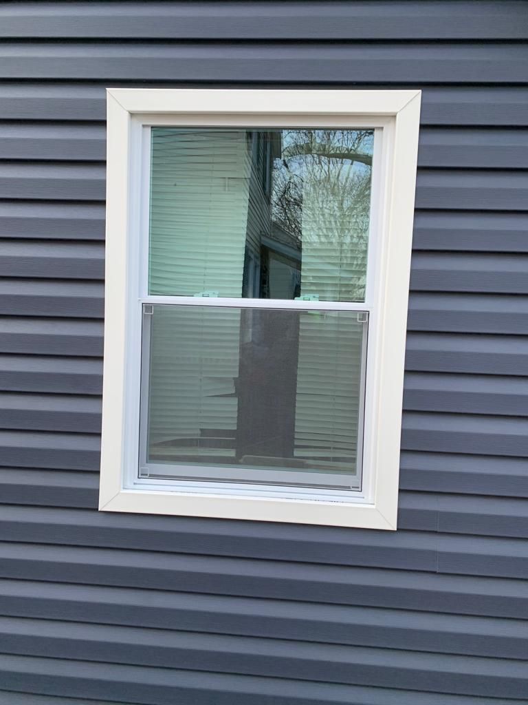 White-trimmed window with blinds on dark gray siding.