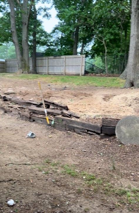 Collapsed stone wall in a wooded yard, with a yellow tool leaning against the rubble