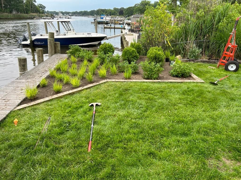 Lakeside yard with fresh green lawn, new shrubs, and a docked boat by the water