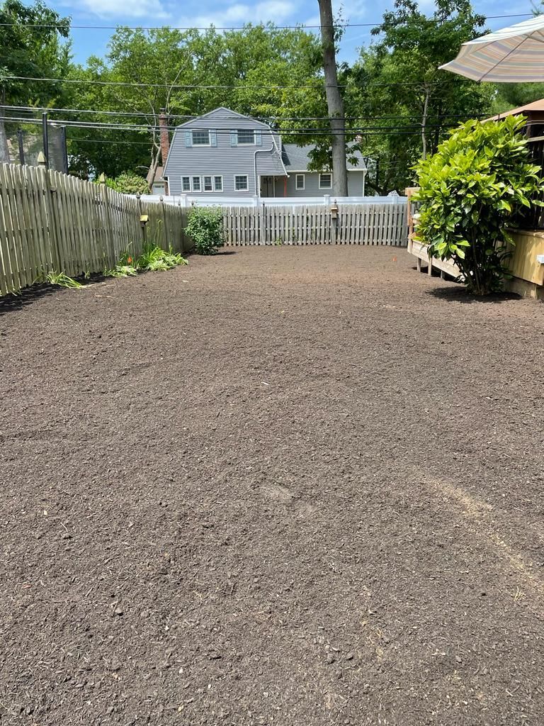 Gravel driveway leading to a white house, bordered by fences and green trees on a sunny day