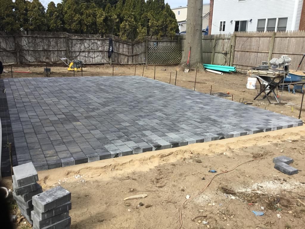 Partially paved backyard with gray pavers, sandy edges, and construction tools in the background