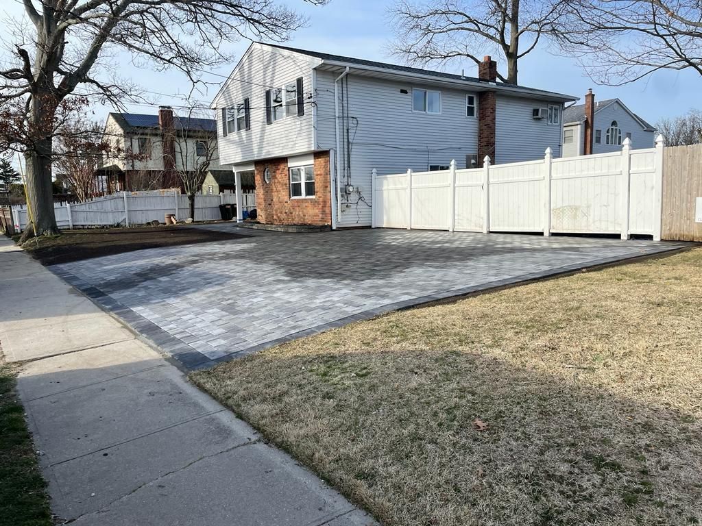 Residential house with a paved driveway, white fence, and leafless trees on a sunny day