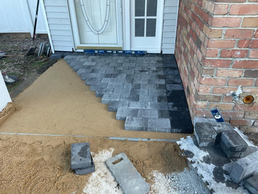 Partially finished front entry walkway with paver and gravel work beside a brick wall