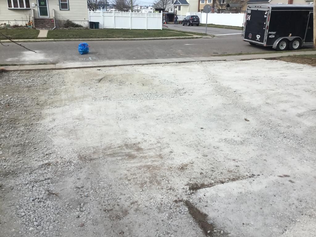 Concrete driveway beside a street, with a blue ball near the curb and a trailer parked at right.