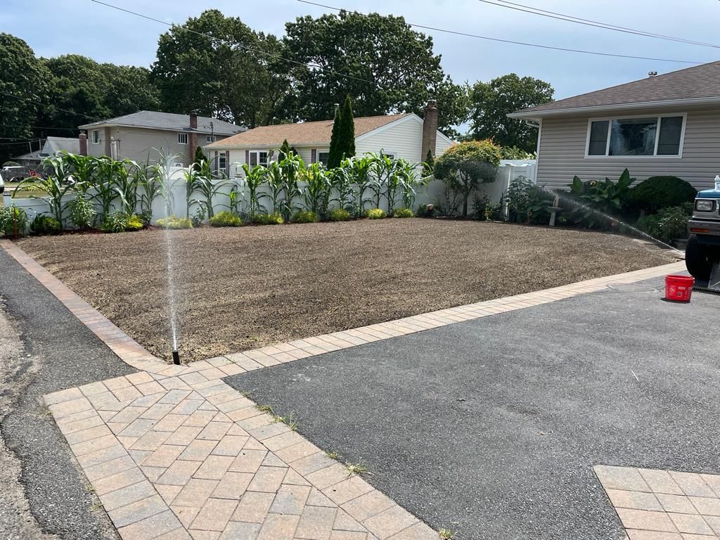 Front yard with fresh gravel soil, paver walkway, and a white fence in a suburban neighborhood