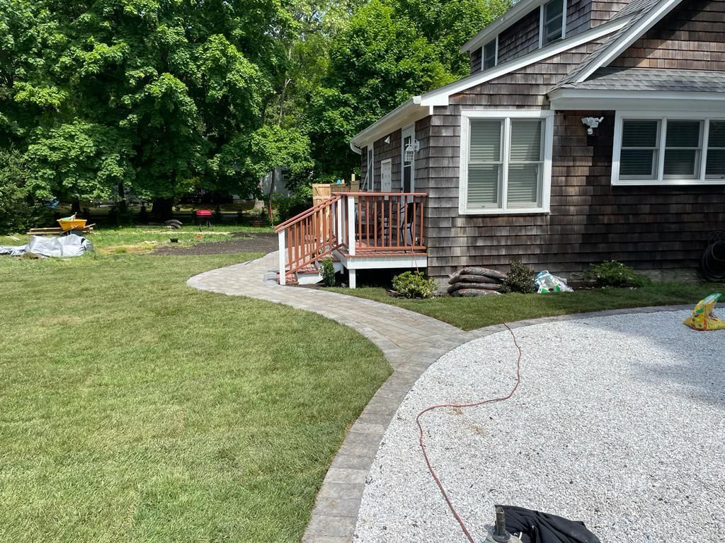 House exterior with a curved gravel walkway, wooden porch, and green lawn surrounded by trees.