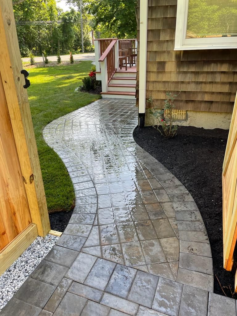 Stone walkway with wet pavers beside a house, leading from a wooden gate to a small porch.