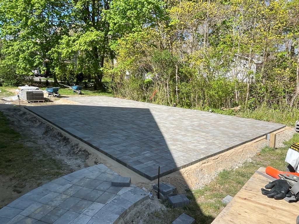 Small concrete patio/slab in a yard, with a triangular shadow and trees in the background.