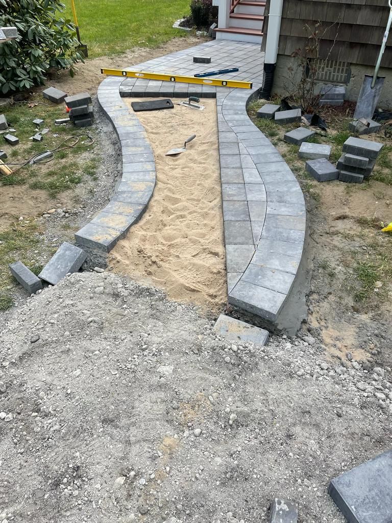Partially built curved stone walkway with sand base in a backyard work area