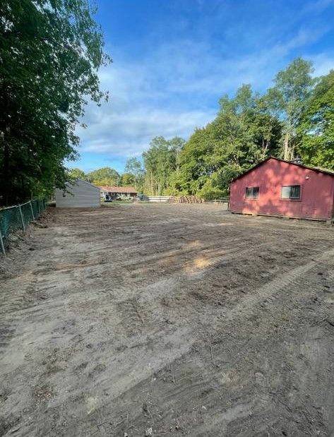 Dirt lot beside trees and a red barn-like building under a blue sky.