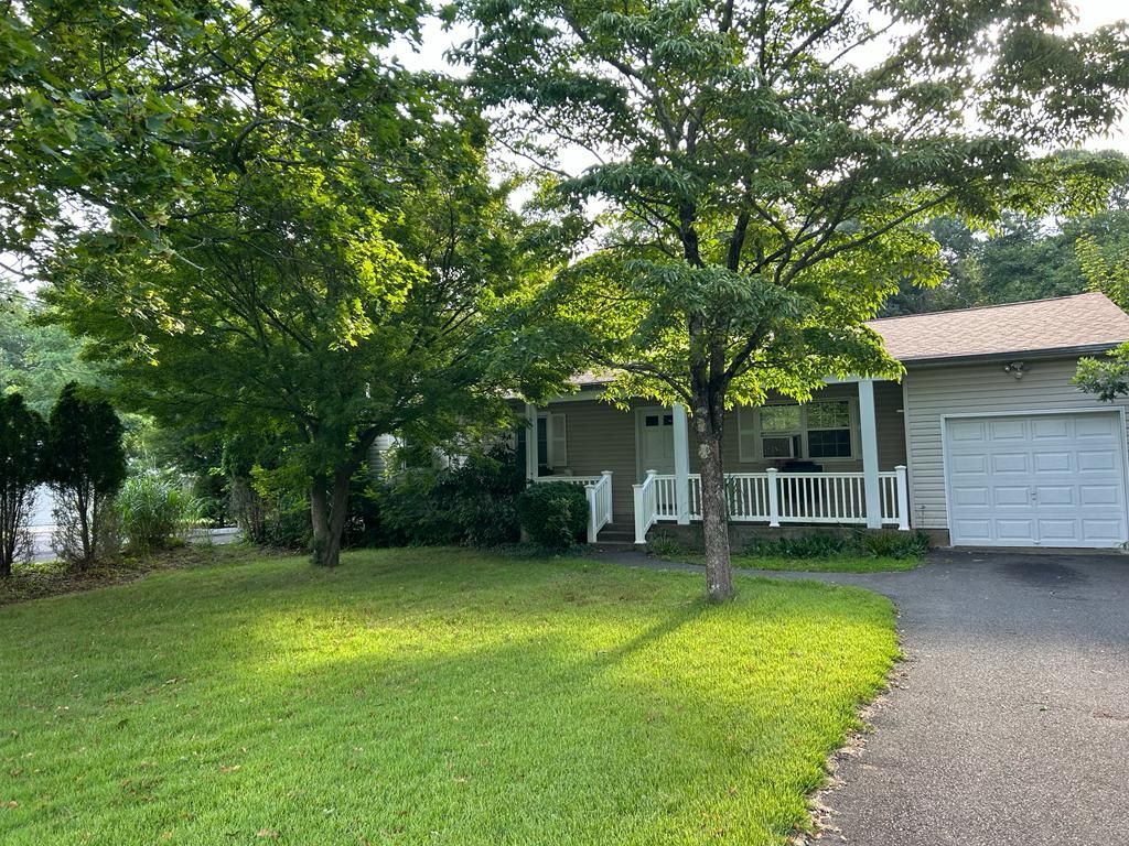 Tree-shaded suburban house with a white porch and garage, beside a green lawn and driveway