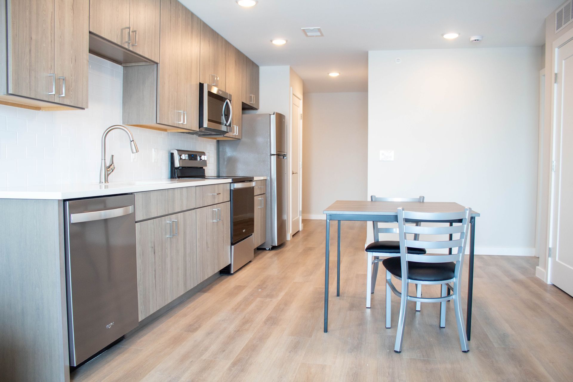 Modern kitchen with wood cabinets, stainless steel appliances, and a small table with chairs.
