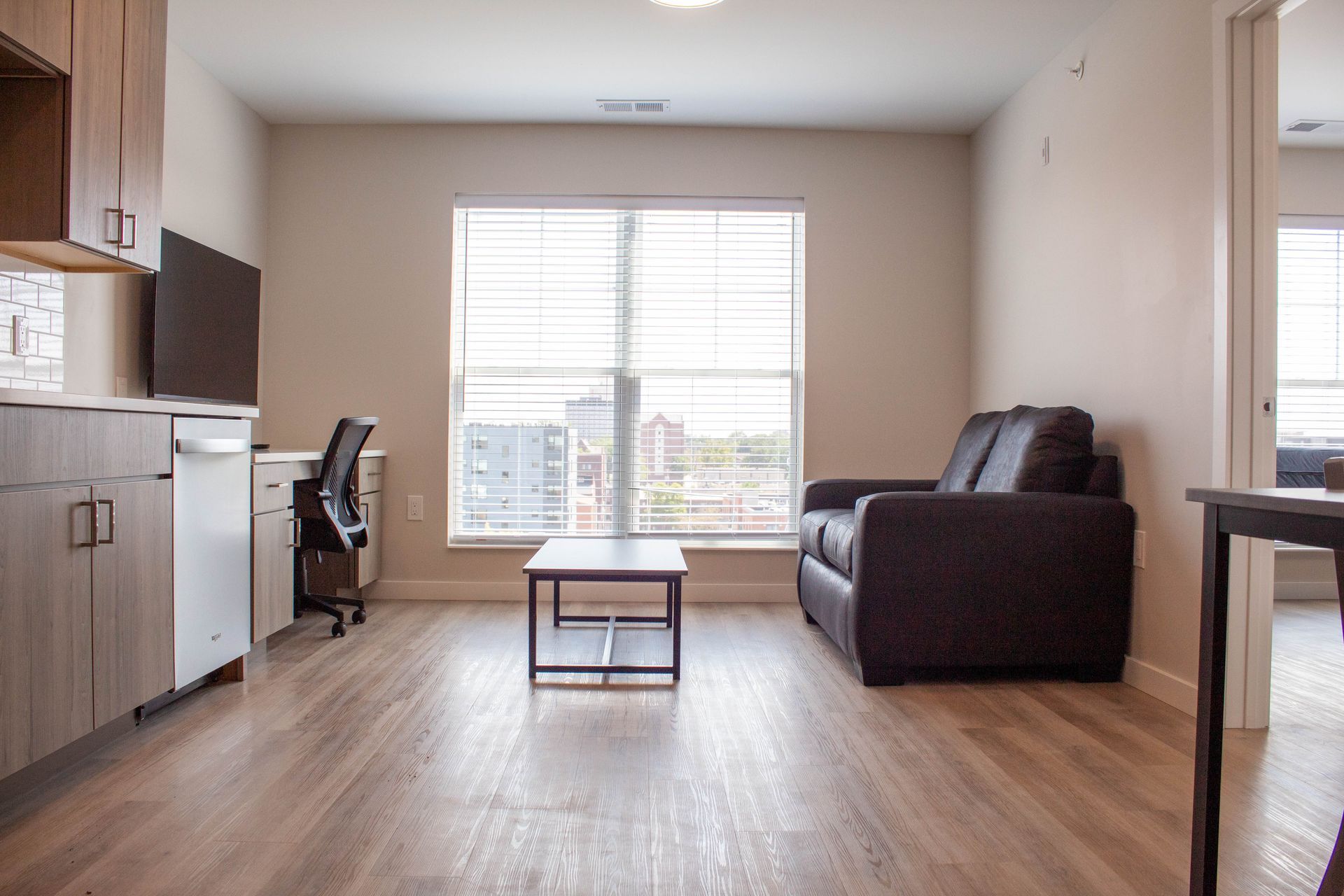 Modern living room with a brown couch, window, desk, and cabinets.